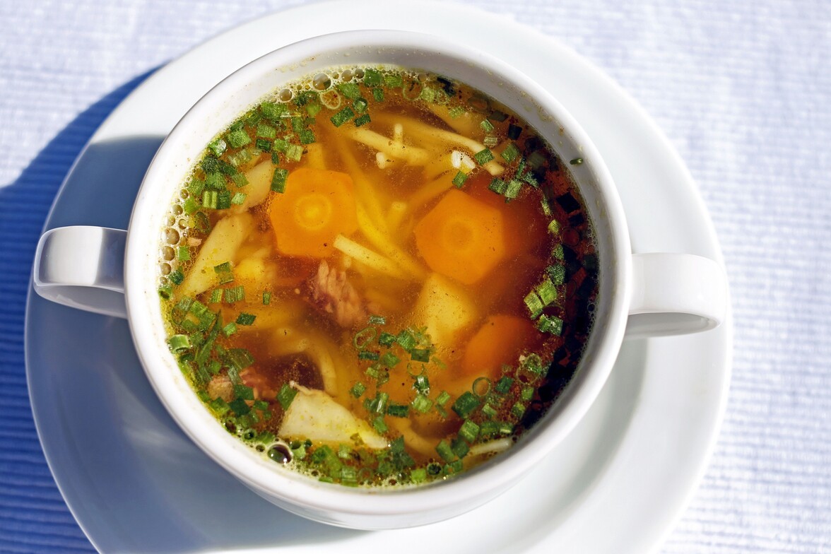 White bowl on white plate filled with chicken soup