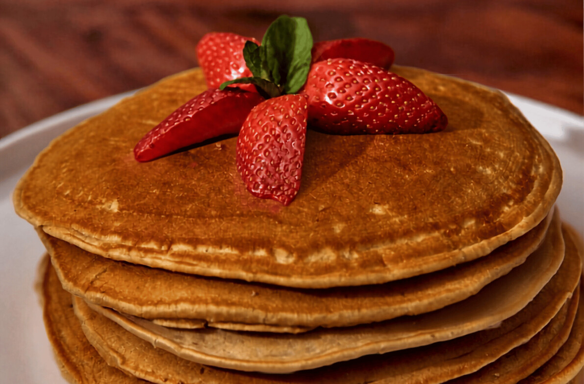 Beautiful einkorn pancakes stacked up with maple syrup and strawberries on top